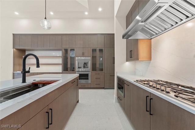 kitchen featuring hanging light fixtures, appliances with stainless steel finishes, sink, backsplash, and wall chimney range hood