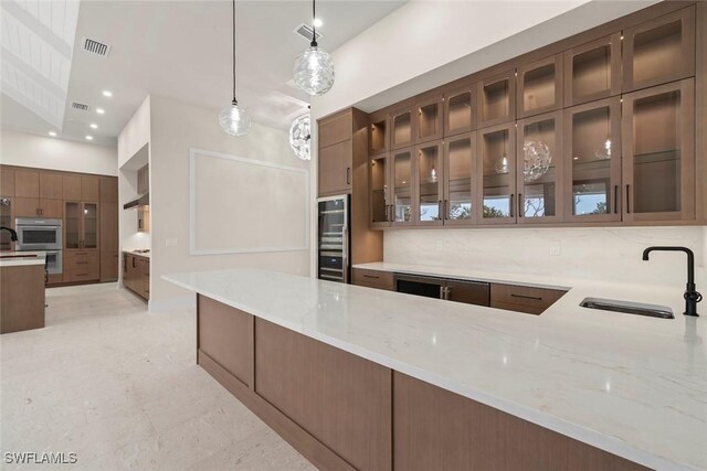 kitchen featuring sink, kitchen peninsula, pendant lighting, backsplash, and light stone counters