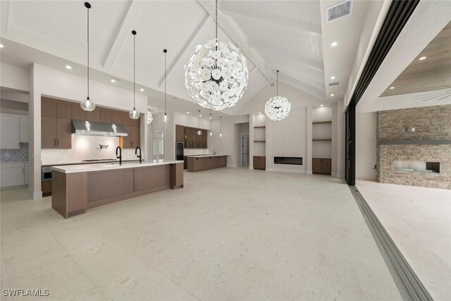 kitchen featuring beamed ceiling, a stone fireplace, tasteful backsplash, wall chimney range hood, and decorative light fixtures