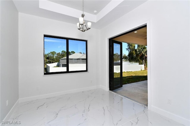 empty room with a tray ceiling and a notable chandelier