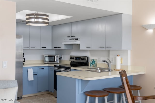 kitchen with appliances with stainless steel finishes, light tile patterned floors, sink, blue cabinets, and a breakfast bar area