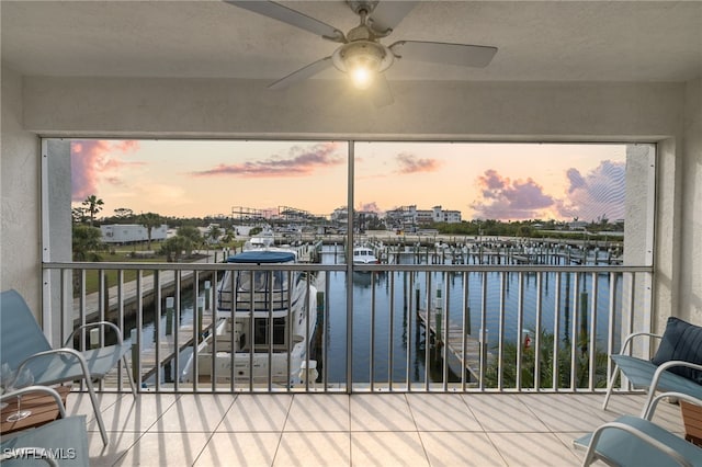 balcony at dusk featuring a water view and ceiling fan