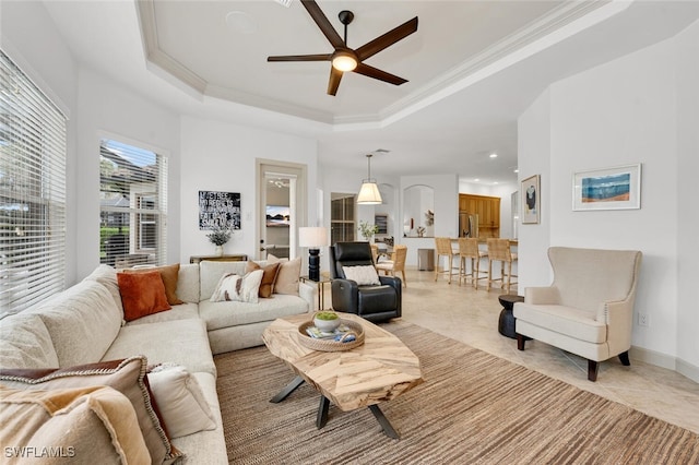 living room with a raised ceiling, ceiling fan, and crown molding