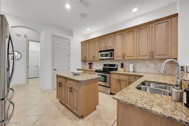 kitchen with light stone countertops, a kitchen island, stainless steel appliances, decorative backsplash, and sink