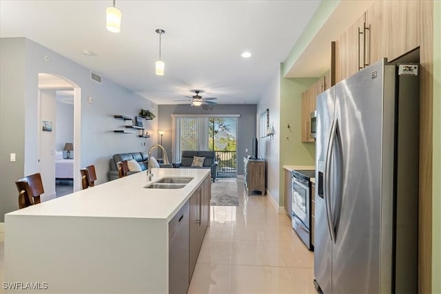 kitchen with light tile patterned floors, an island with sink, appliances with stainless steel finishes, decorative light fixtures, and sink