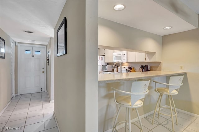 kitchen with a breakfast bar area, white cabinetry, range, light tile patterned floors, and kitchen peninsula