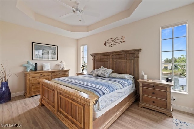 bedroom with ceiling fan, light hardwood / wood-style floors, and a raised ceiling