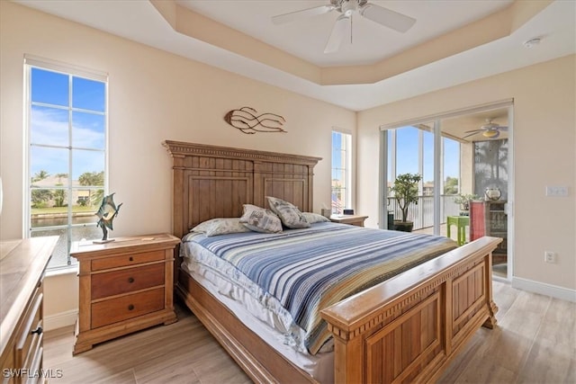 bedroom with ceiling fan, access to exterior, light hardwood / wood-style flooring, and a raised ceiling