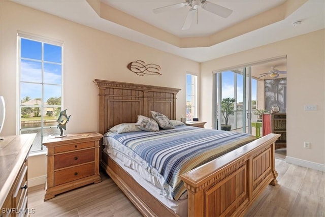 bedroom featuring ceiling fan, multiple windows, a tray ceiling, and access to outside