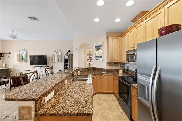 kitchen featuring kitchen peninsula, appliances with stainless steel finishes, light brown cabinets, dark stone countertops, and sink