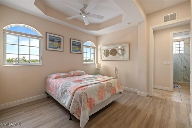 bedroom featuring ceiling fan, a tray ceiling, and light hardwood / wood-style flooring