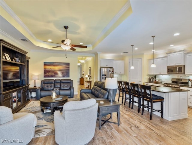 living room with ceiling fan, a raised ceiling, and crown molding