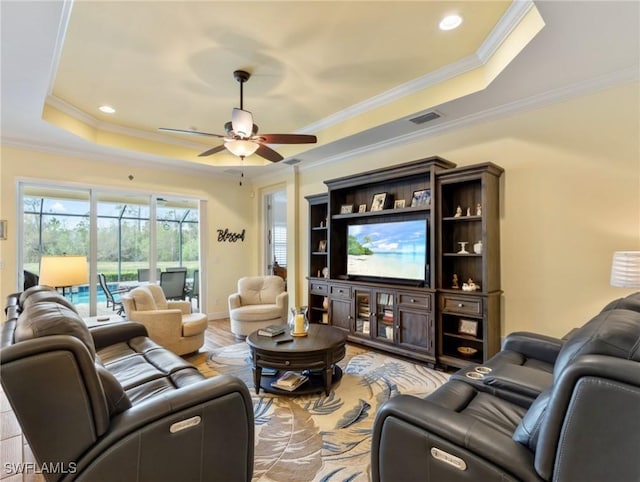 living room featuring light wood-type flooring, ceiling fan, ornamental molding, and a tray ceiling