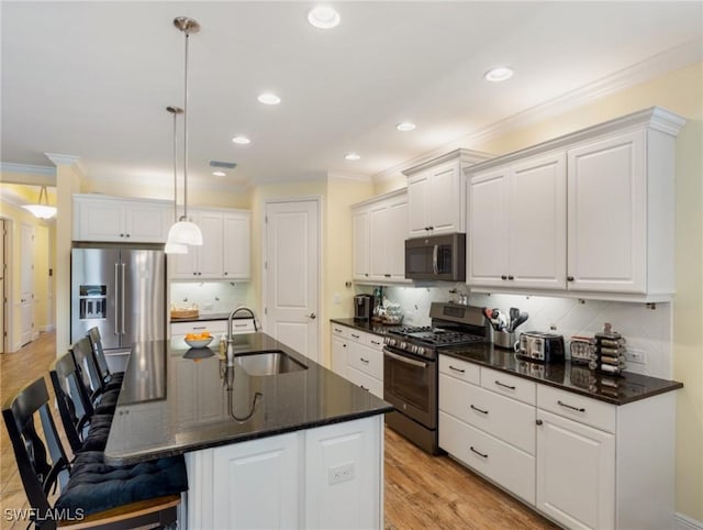 kitchen featuring white cabinetry, sink, decorative light fixtures, stainless steel appliances, and a center island with sink