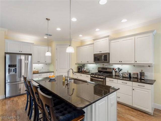 kitchen with hanging light fixtures, stainless steel appliances, a kitchen island with sink, and tasteful backsplash