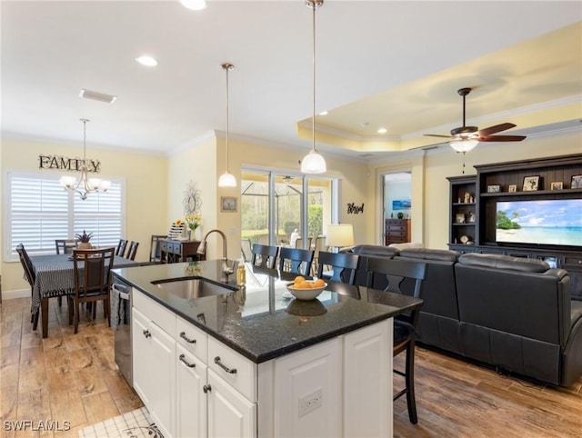 kitchen featuring white cabinetry, a kitchen island with sink, sink, light wood-type flooring, and dark stone counters