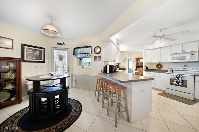 kitchen featuring a kitchen bar, light tile patterned floors, kitchen peninsula, white appliances, and white cabinets