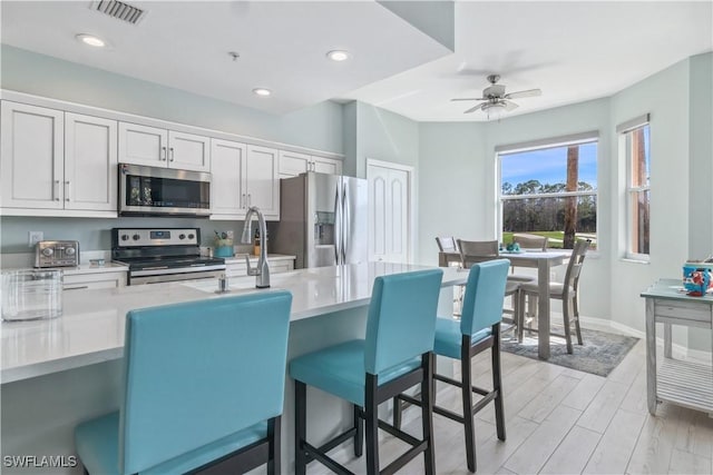 kitchen featuring ceiling fan, white cabinets, a kitchen breakfast bar, and appliances with stainless steel finishes