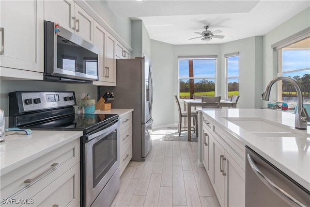 kitchen with sink, white cabinets, light stone countertops, light hardwood / wood-style floors, and stainless steel appliances