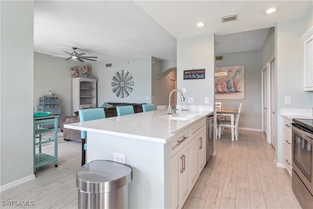 kitchen featuring stainless steel appliances, white cabinets, sink, an island with sink, and a breakfast bar area