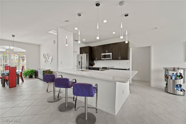 kitchen featuring appliances with stainless steel finishes, pendant lighting, a breakfast bar area, light stone counters, and dark brown cabinets