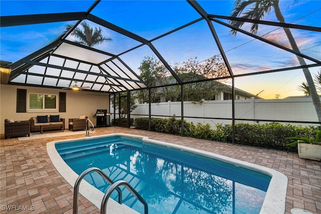 pool at dusk with a grill, an outdoor hangout area, a patio area, and glass enclosure