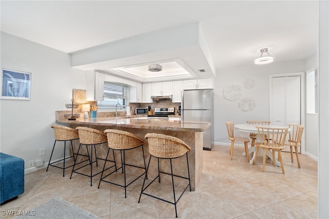 kitchen featuring a breakfast bar, white cabinetry, backsplash, kitchen peninsula, and stainless steel appliances