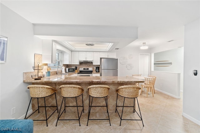 kitchen featuring a breakfast bar area, appliances with stainless steel finishes, white cabinets, a raised ceiling, and kitchen peninsula