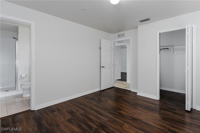 unfurnished bedroom with ensuite bathroom, dark hardwood / wood-style floors, a closet, and a spacious closet