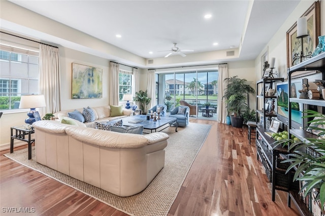 living room featuring hardwood / wood-style flooring, a raised ceiling, and ceiling fan