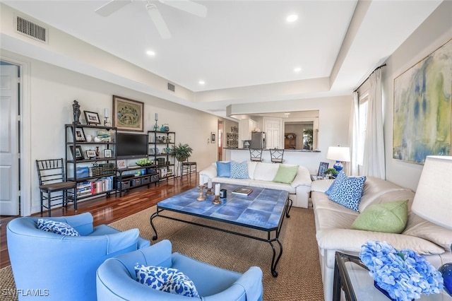 living room featuring dark wood-type flooring, ceiling fan, and a tray ceiling