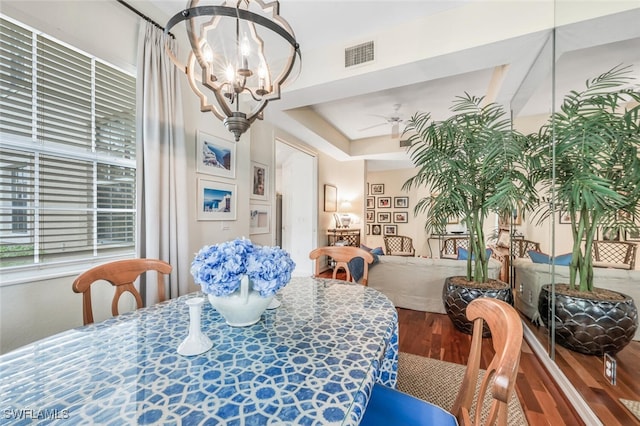 dining room with ceiling fan with notable chandelier, wood-type flooring, and a raised ceiling