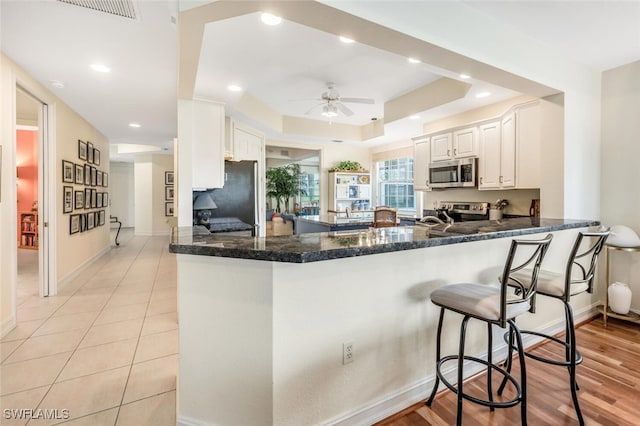 kitchen with appliances with stainless steel finishes, a tray ceiling, kitchen peninsula, and white cabinets