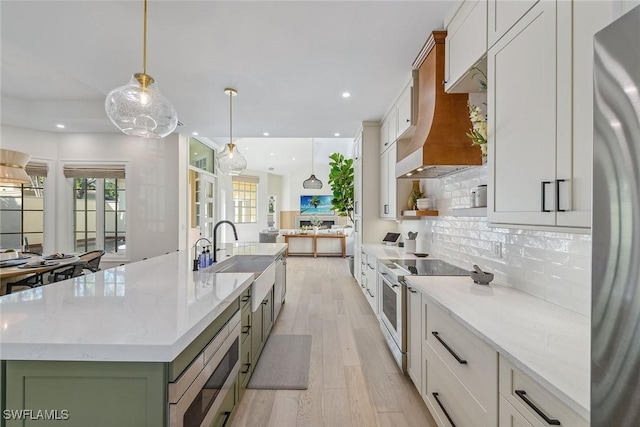 kitchen featuring white cabinets, pendant lighting, stainless steel appliances, and a center island with sink