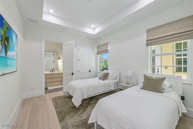 bedroom featuring ensuite bath, sink, a tray ceiling, and hardwood / wood-style flooring