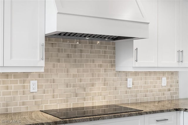 kitchen with white cabinetry, custom exhaust hood, black electric stovetop, tasteful backsplash, and dark stone countertops