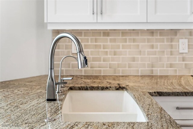 room details with tasteful backsplash, white cabinets, sink, and light stone counters