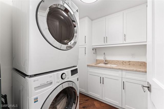 laundry area featuring stacked washer and dryer, dark hardwood / wood-style floors, sink, and cabinets