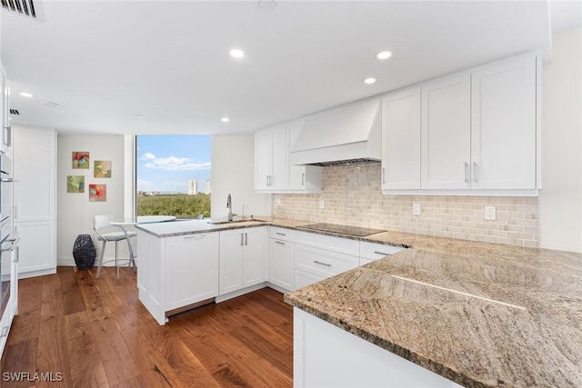 kitchen featuring premium range hood, kitchen peninsula, sink, white cabinets, and black electric cooktop