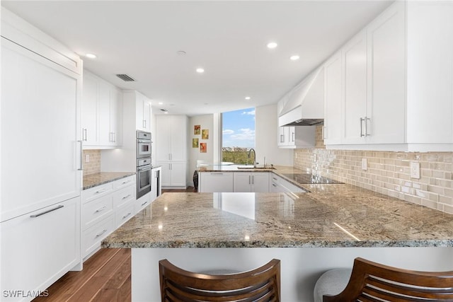 kitchen with premium range hood, white cabinetry, kitchen peninsula, and a breakfast bar area