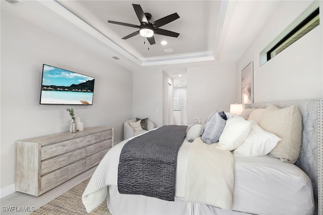 bedroom featuring ensuite bathroom, ceiling fan, and a raised ceiling