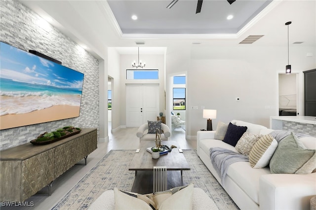 living room with ceiling fan with notable chandelier, crown molding, a raised ceiling, and a towering ceiling