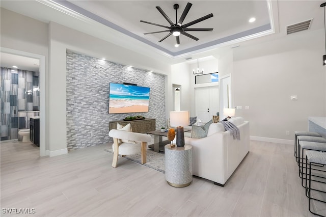 living room with a tray ceiling, light wood-type flooring, and ceiling fan with notable chandelier