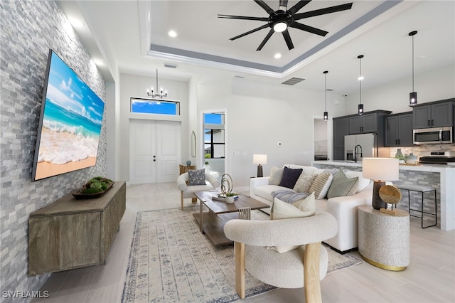 living room featuring ceiling fan with notable chandelier, light hardwood / wood-style flooring, a raised ceiling, and a towering ceiling