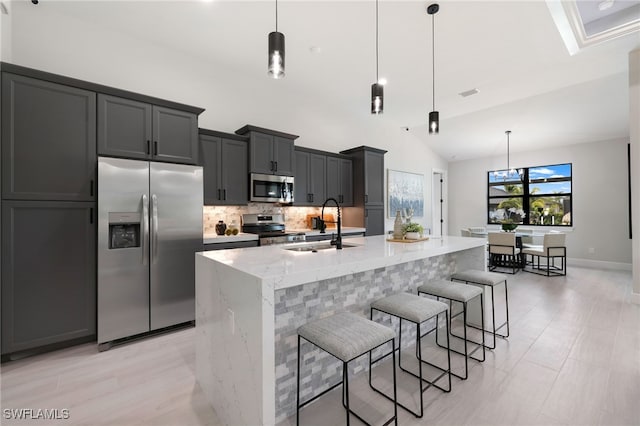 kitchen with appliances with stainless steel finishes, an island with sink, light stone countertops, decorative light fixtures, and sink