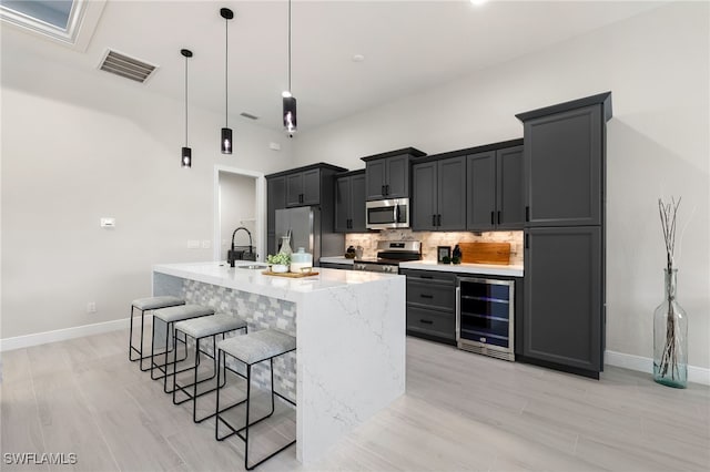 kitchen with appliances with stainless steel finishes, hanging light fixtures, a breakfast bar area, decorative backsplash, and wine cooler