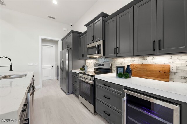 kitchen featuring appliances with stainless steel finishes, sink, light stone counters, wine cooler, and tasteful backsplash