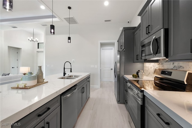 kitchen featuring appliances with stainless steel finishes, gray cabinetry, light stone countertops, pendant lighting, and sink