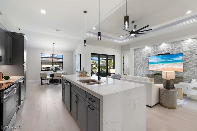 kitchen with a center island with sink, sink, light stone counters, pendant lighting, and a tray ceiling