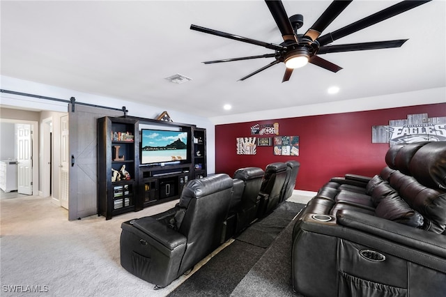 carpeted cinema room with ceiling fan and a barn door